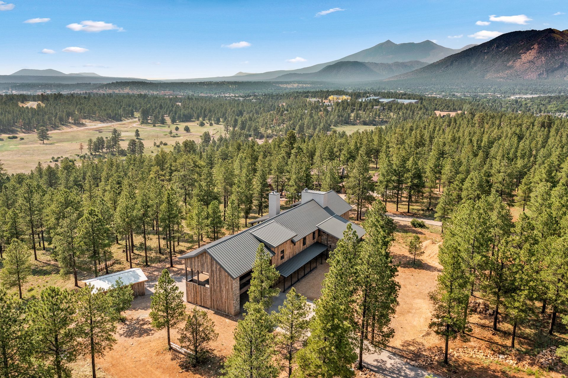 An aerial view of a house in the middle of a forest with mountains in the background.