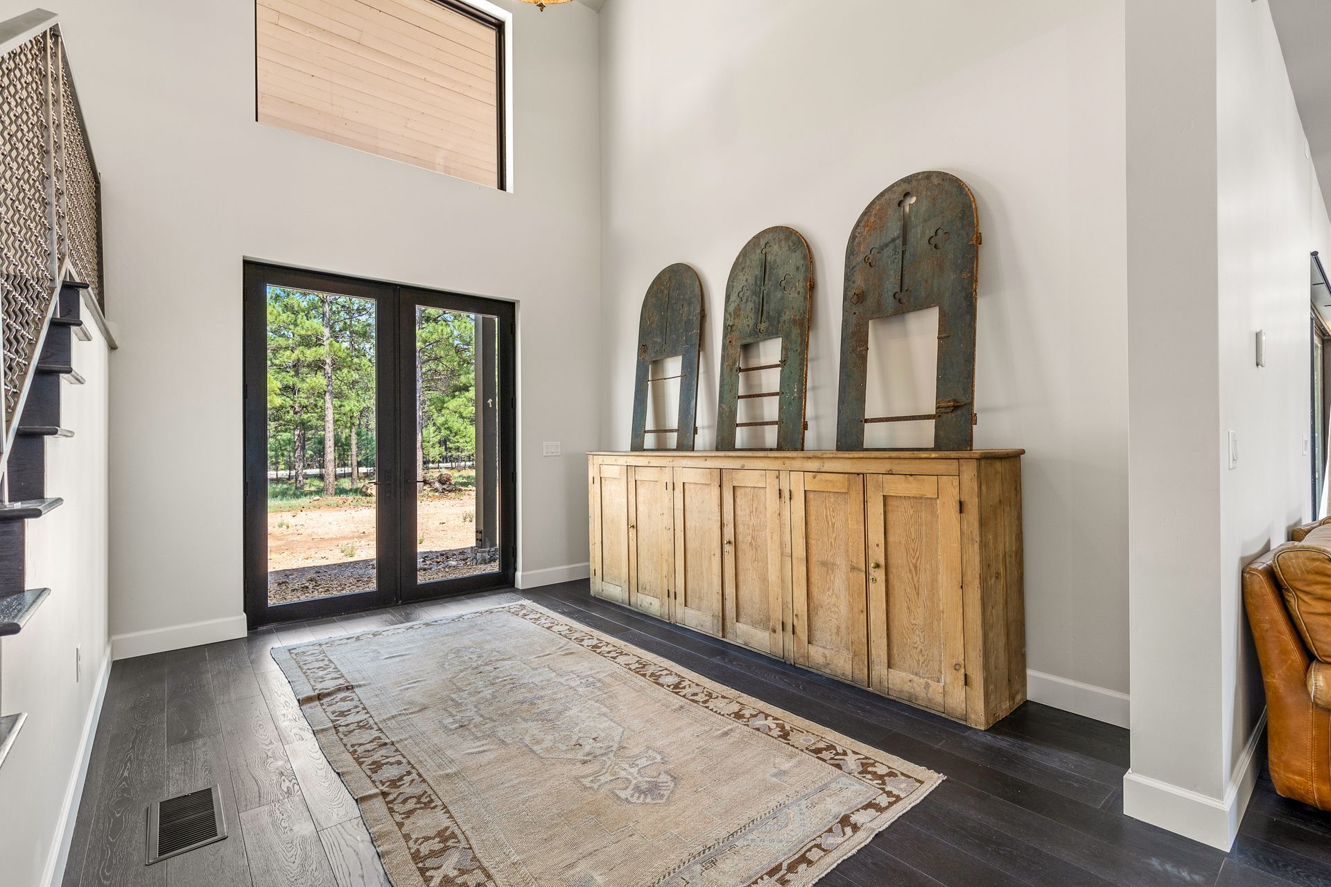 Entryway with dark wood floor, cabinet, antique arches, and glass doors leading to a wooded view.
