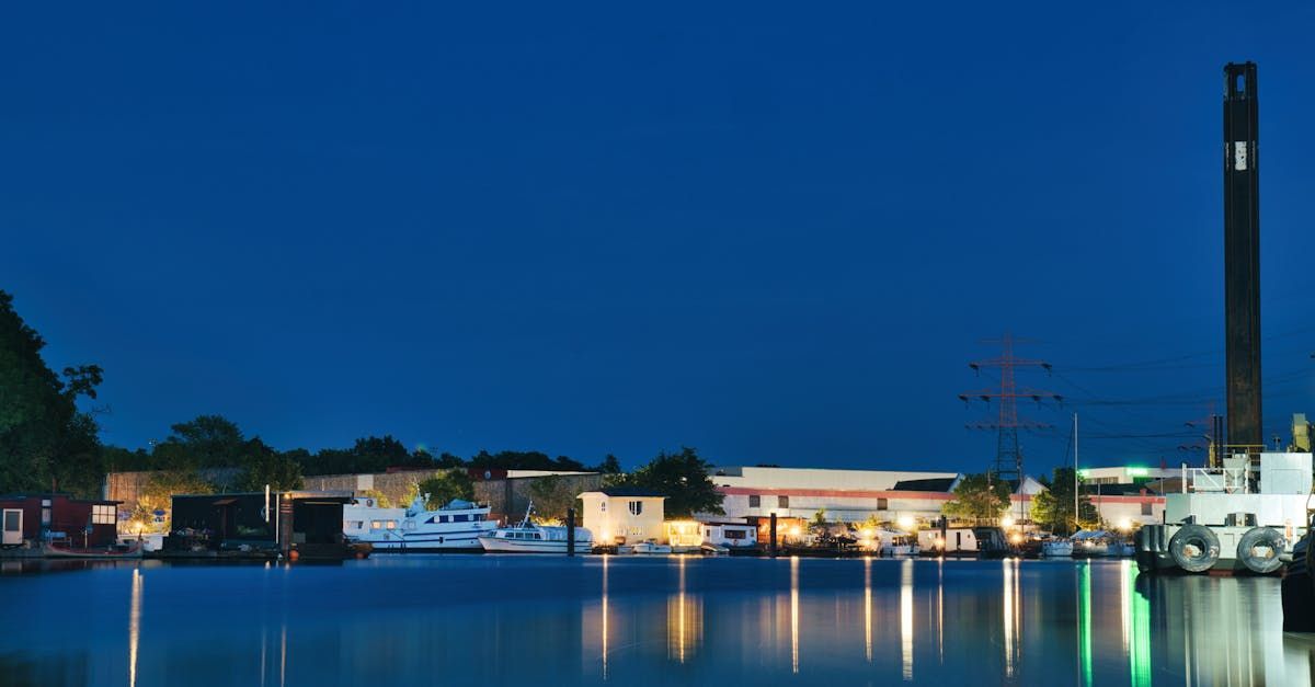 A marina at twilight with boats docked along the shore, reflected in calm, dark water under a deep blue sky.