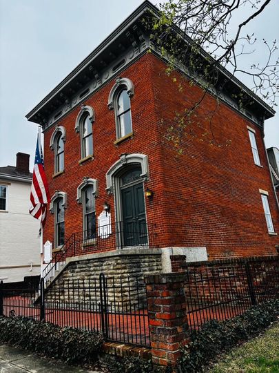A large red brick building with stairs leading up to it and an american flag flying in front of it.
