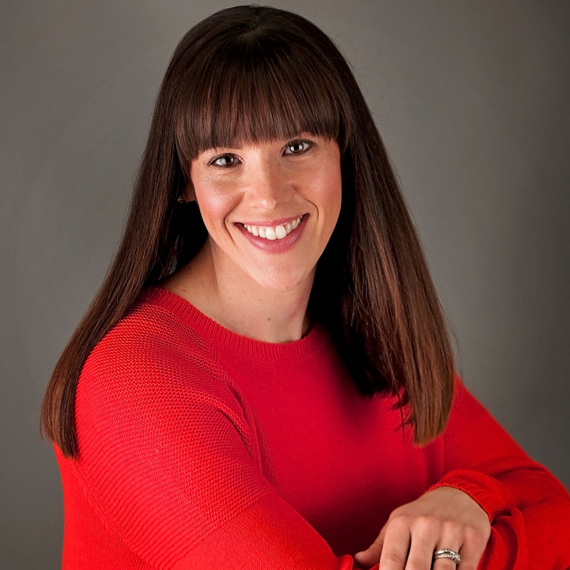 A woman in a red sweater is smiling and wearing a ring on her finger.