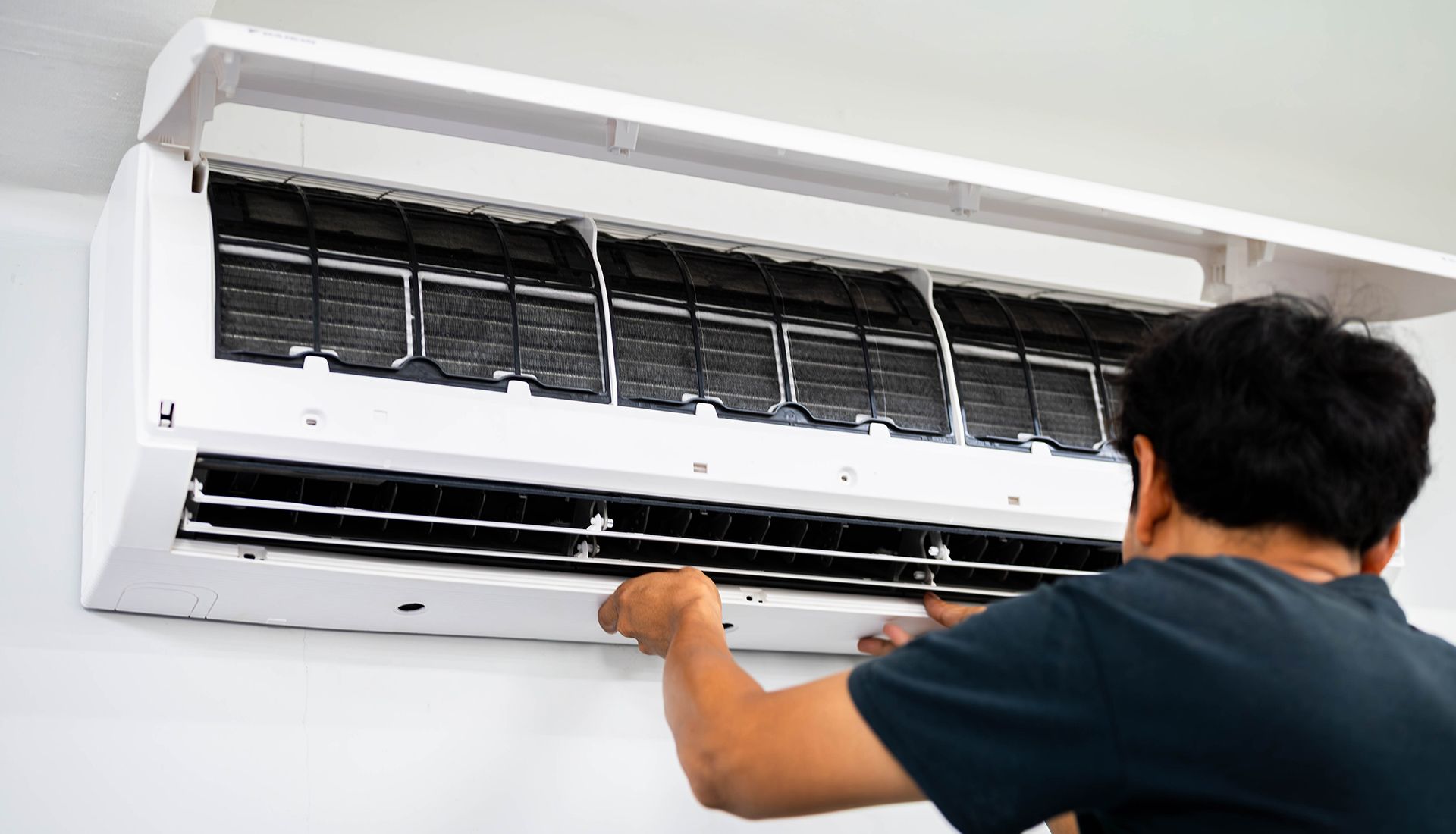 Person removing air filters from a wall-mounted air conditioning unit.