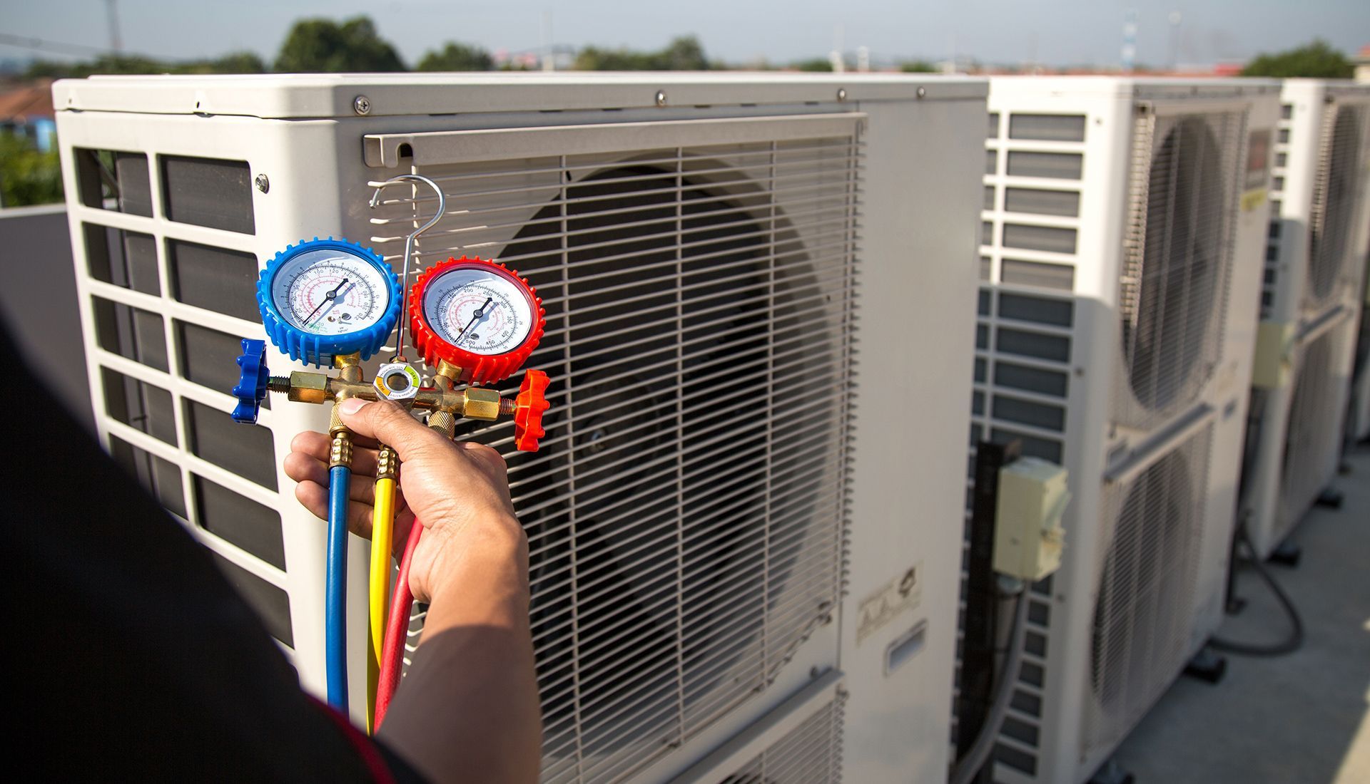 Two HVAC technicians in blue uniforms working on an air conditioning unit.