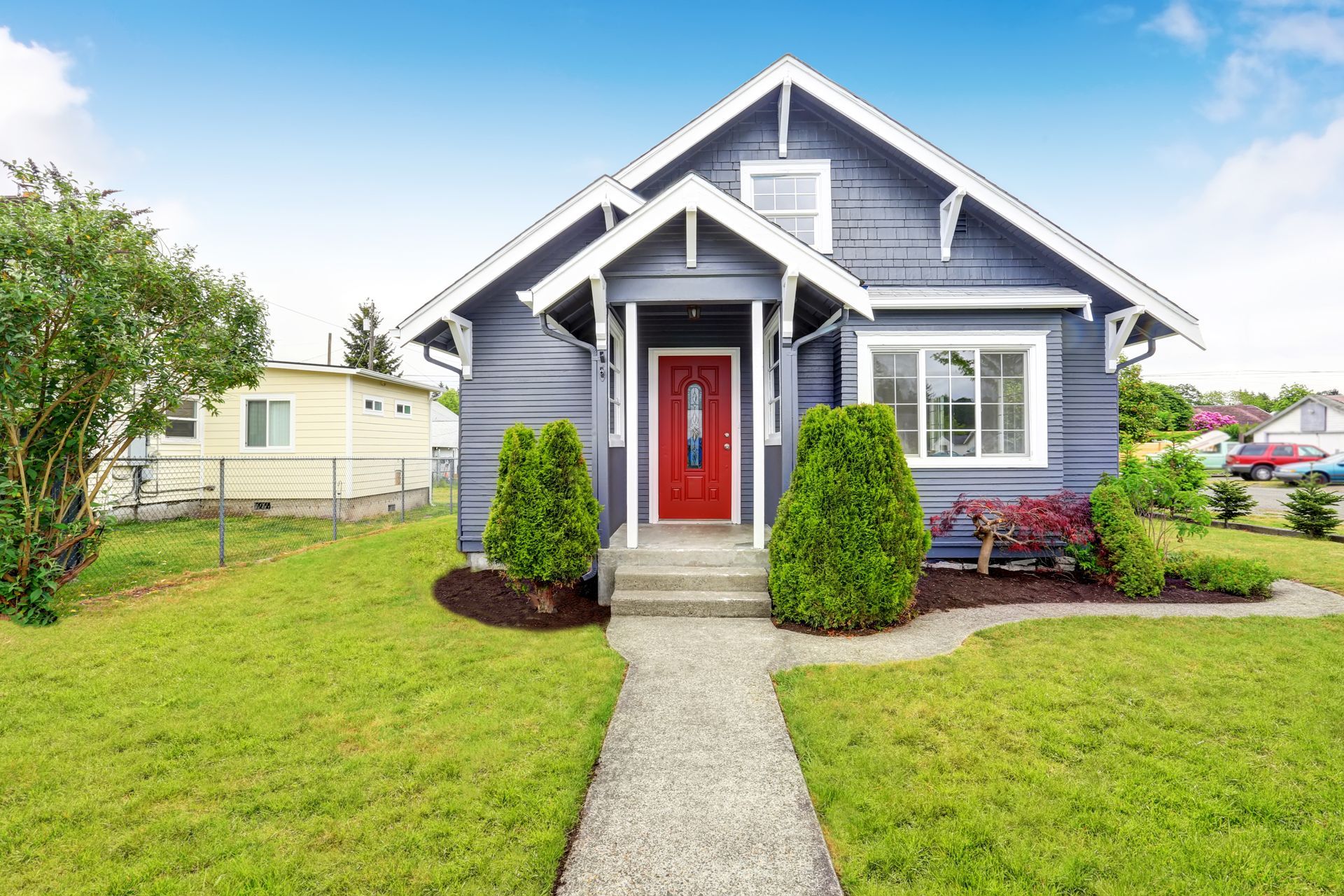 Blue house with red door, white trim, and a walkway through a green lawn.