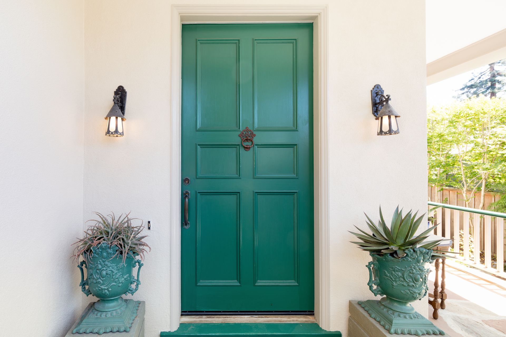 Emerald green front door with sconces, flanked by potted plants, on a white porch.