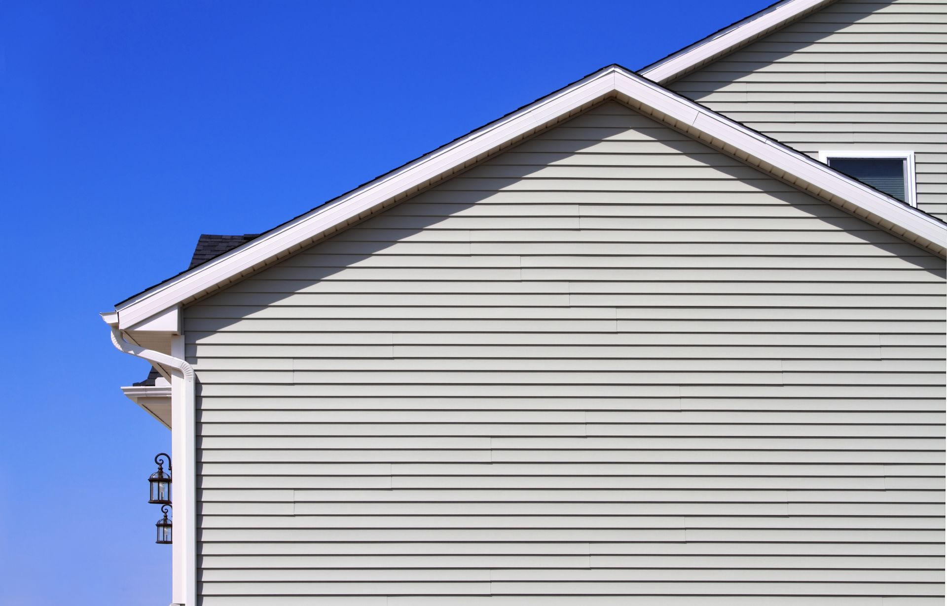 Side of a house with light green siding and white trim against a blue sky.