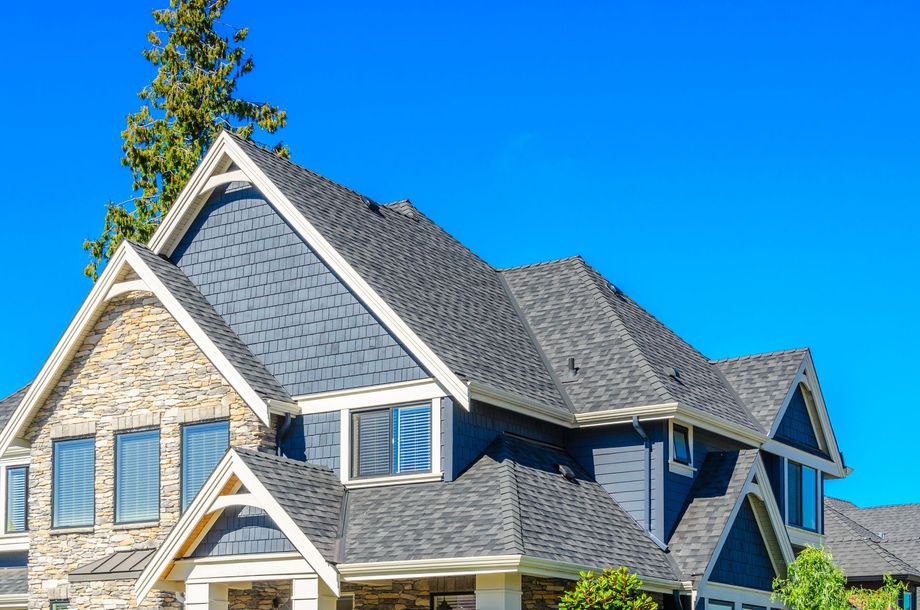 Blue and stone home with dark gray roof against a clear, bright blue sky.