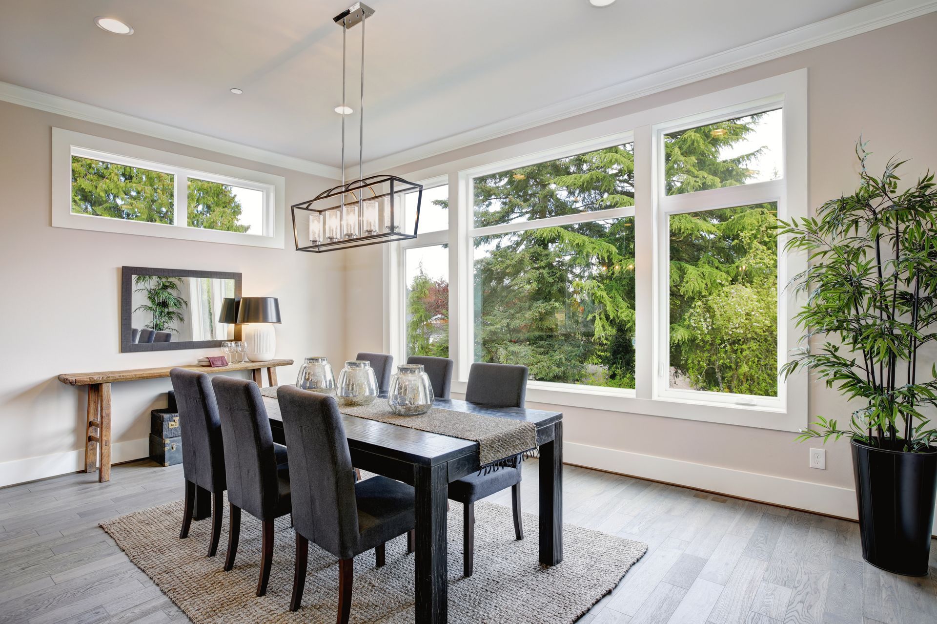Dining room with large windows overlooking trees, table with chairs, and a potted plant.