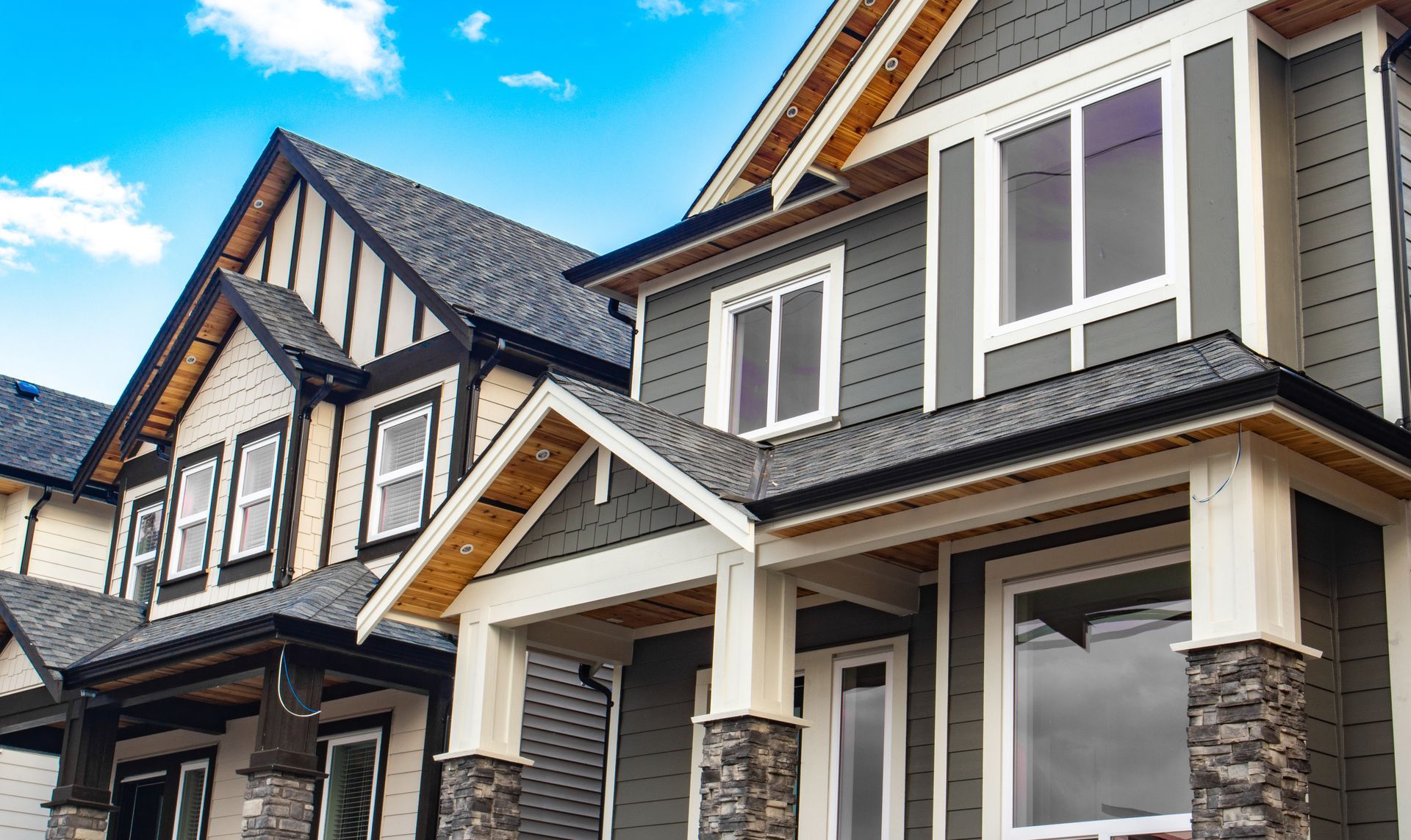Row of modern houses with various exterior styles, gray and cream siding, stone columns, under a blue sky.