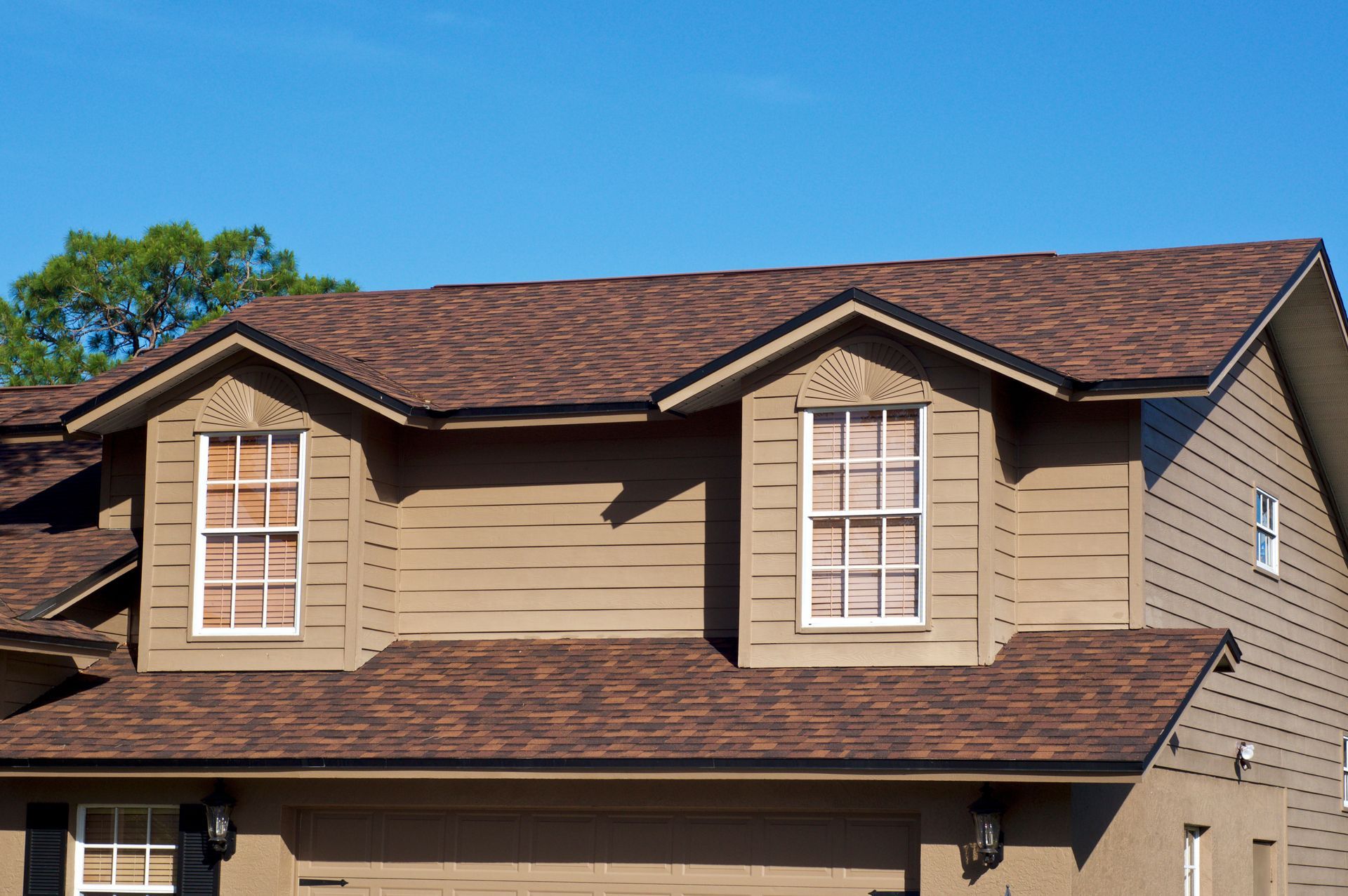 Brown roof and siding on a two-story house with dormer windows against a blue sky.
