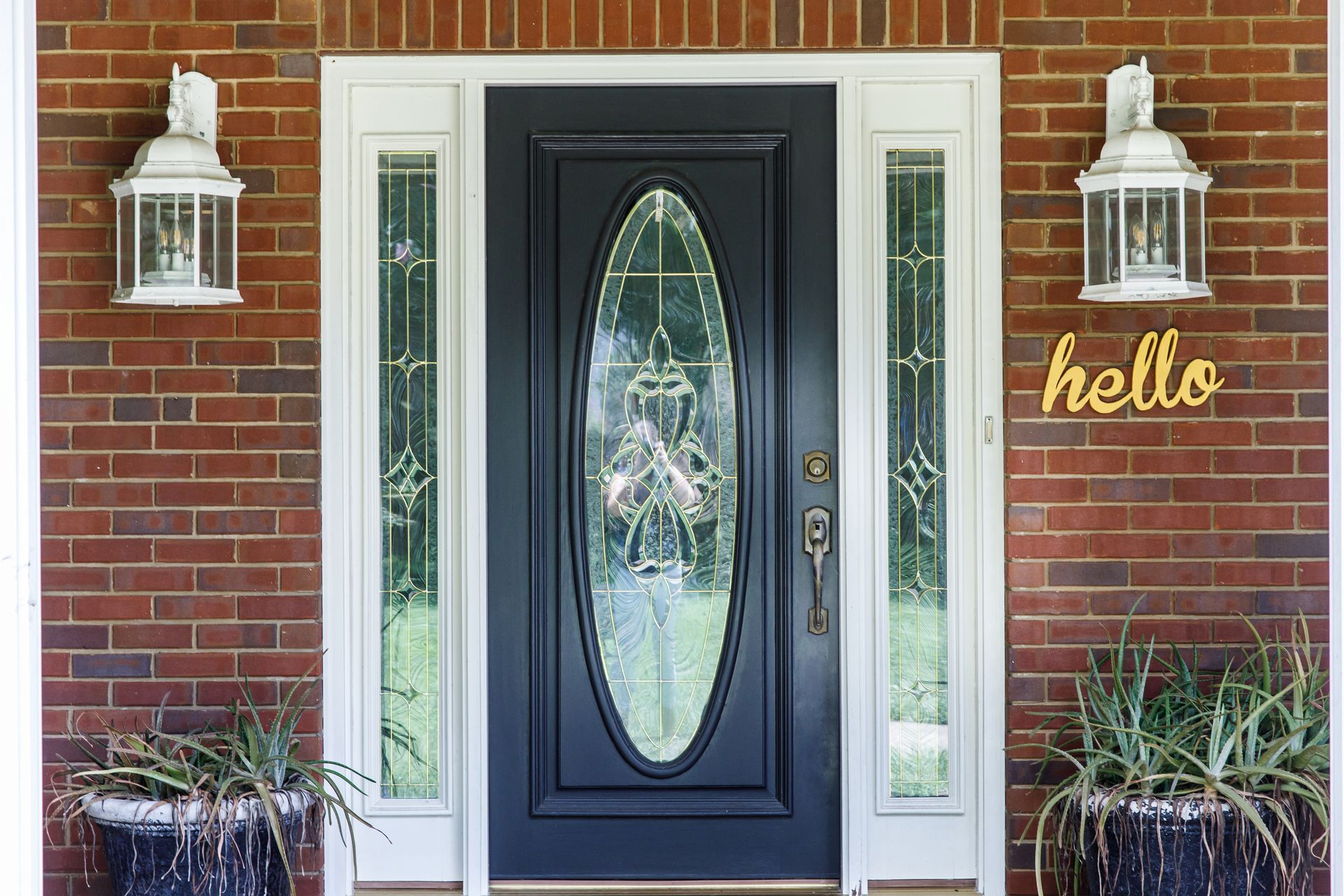Front door with sidelights, brick exterior, and decorative lanterns. 
