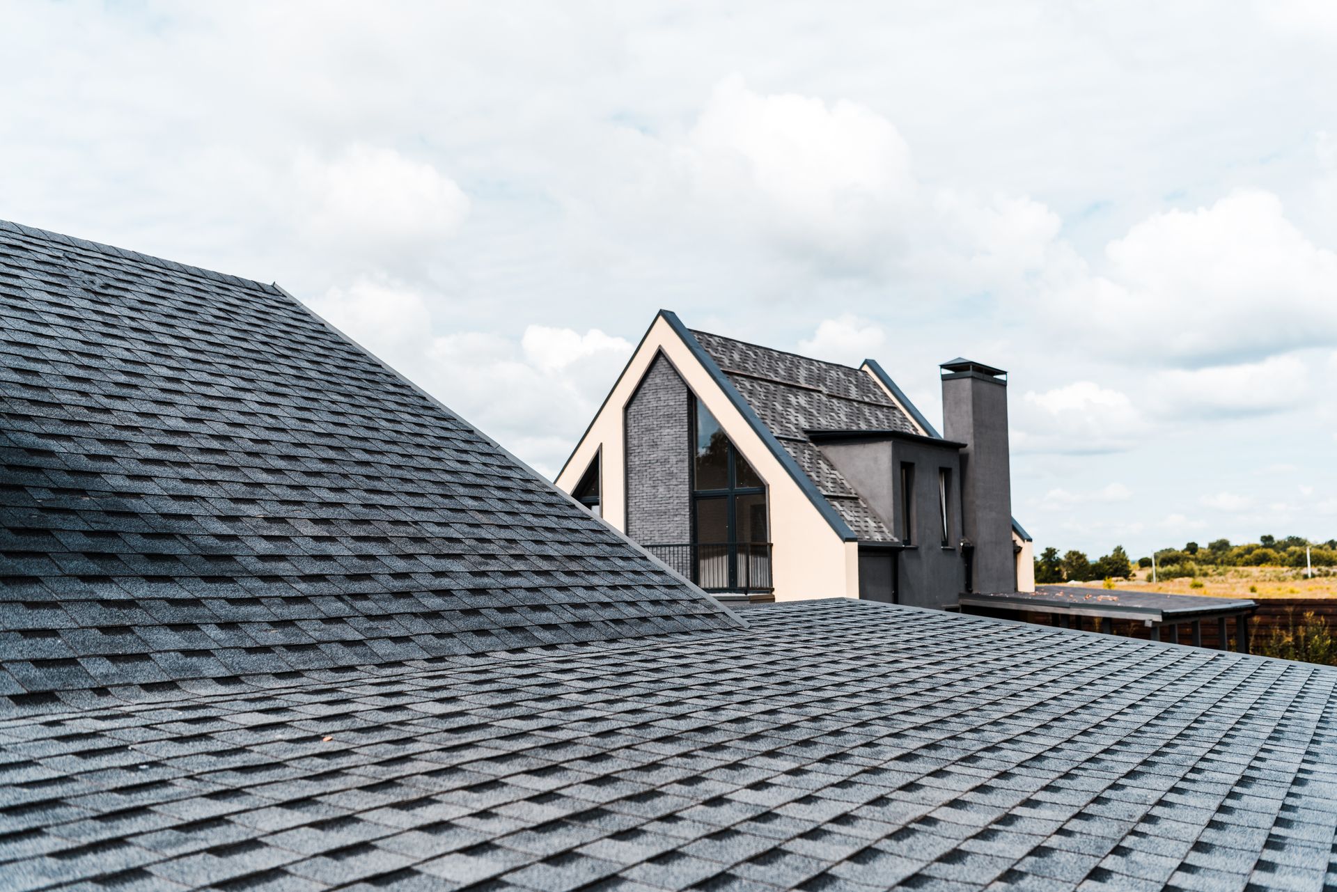 Gray shingled rooftops, with a modern gray and white house in the background. Cloudy sky.