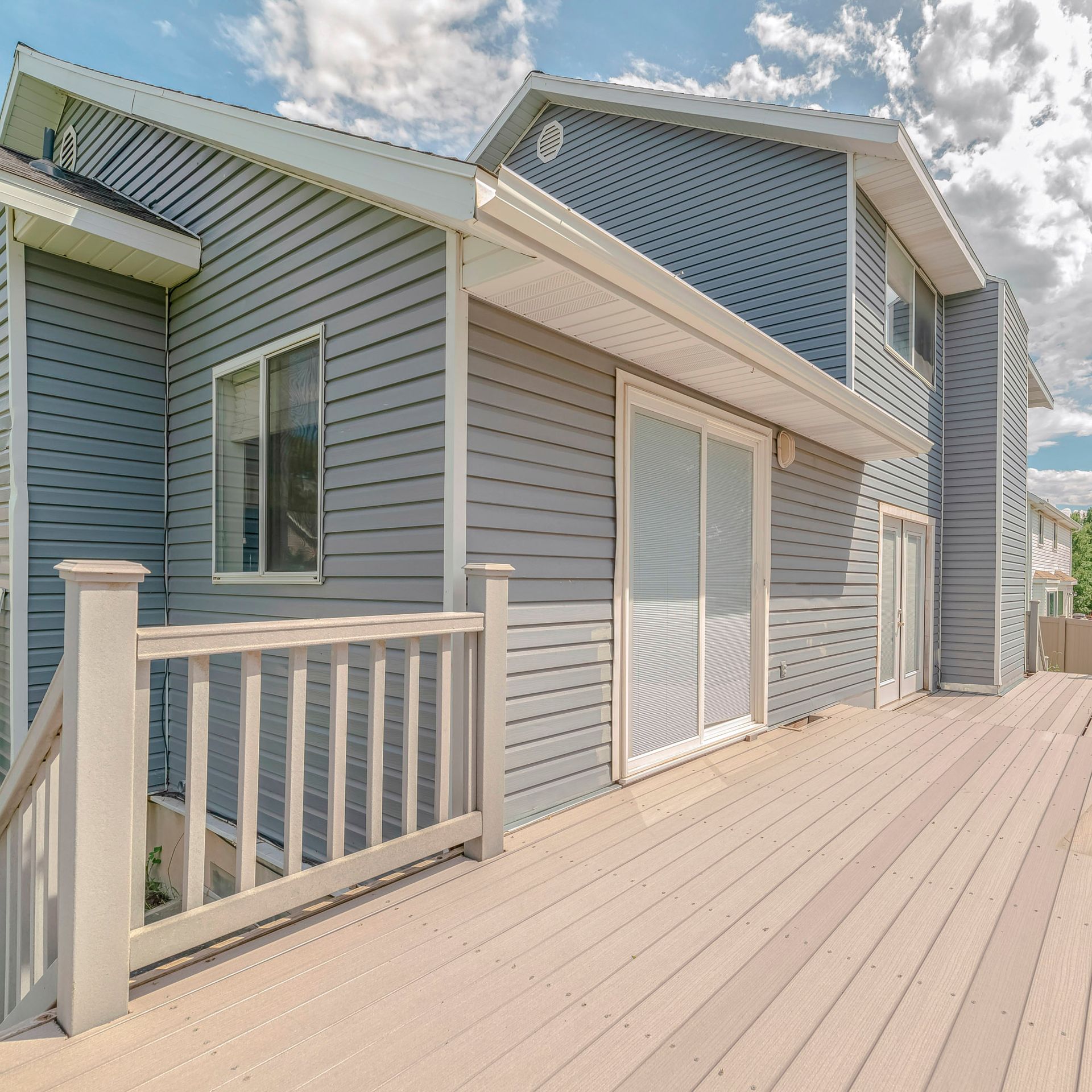 Back of a gray sided house with a wooden deck and a glass sliding door on a sunny day.