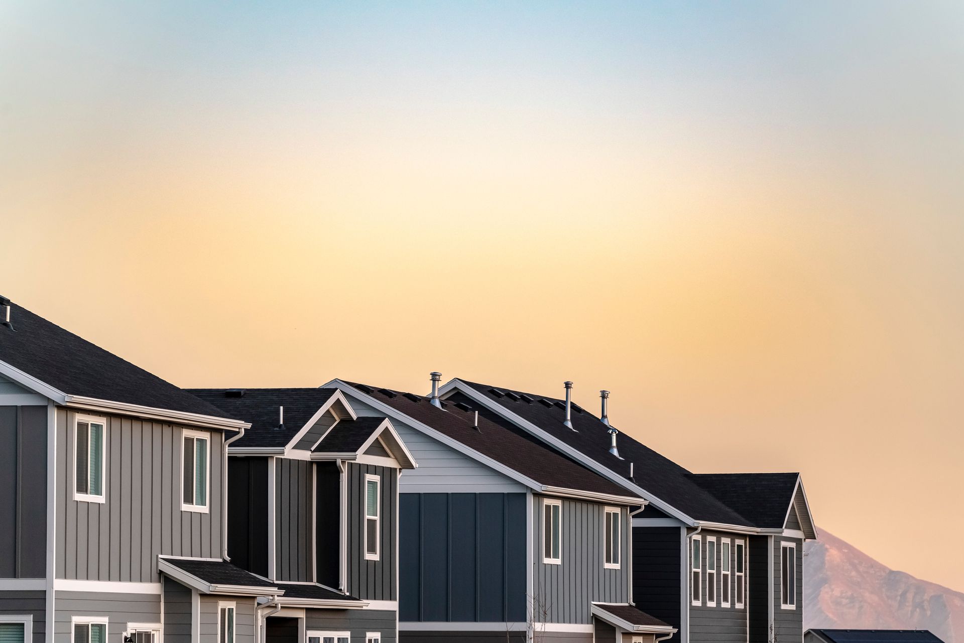 Row of modern townhouses with gray siding and dark roofs under a sunset sky.