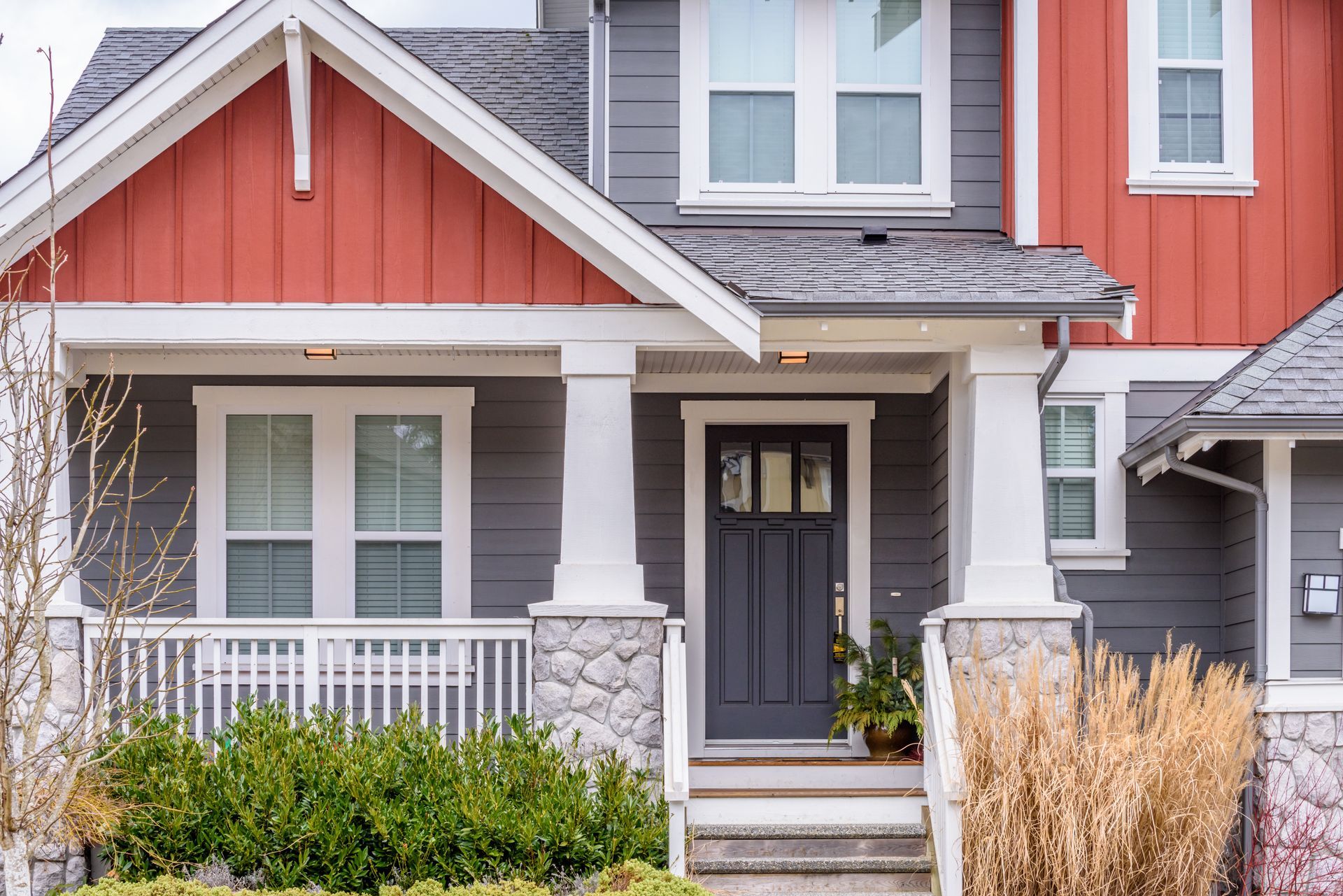 Grey house with red accents, porch, front door, and windows.