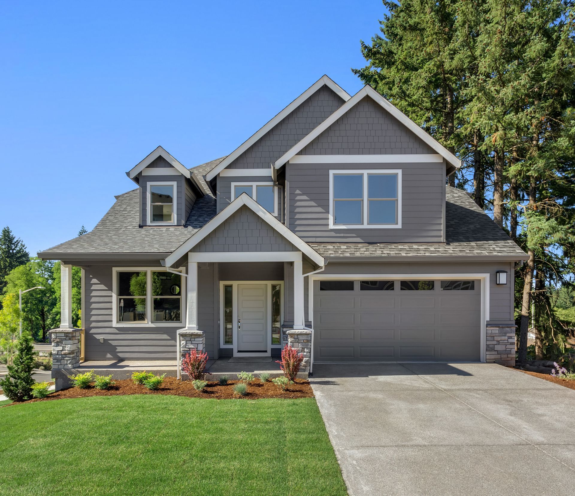 Gray two-story house with a driveway and green lawn on a sunny day.