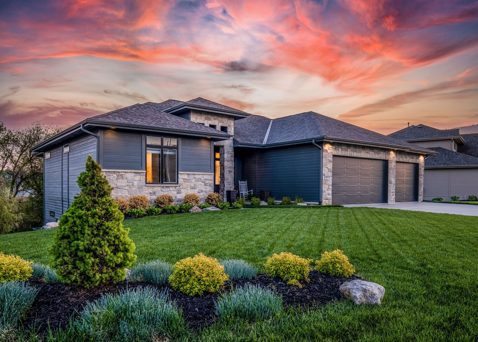 House exterior with a colorful sunset sky; landscaped yard, three-car garage, stone and gray siding.