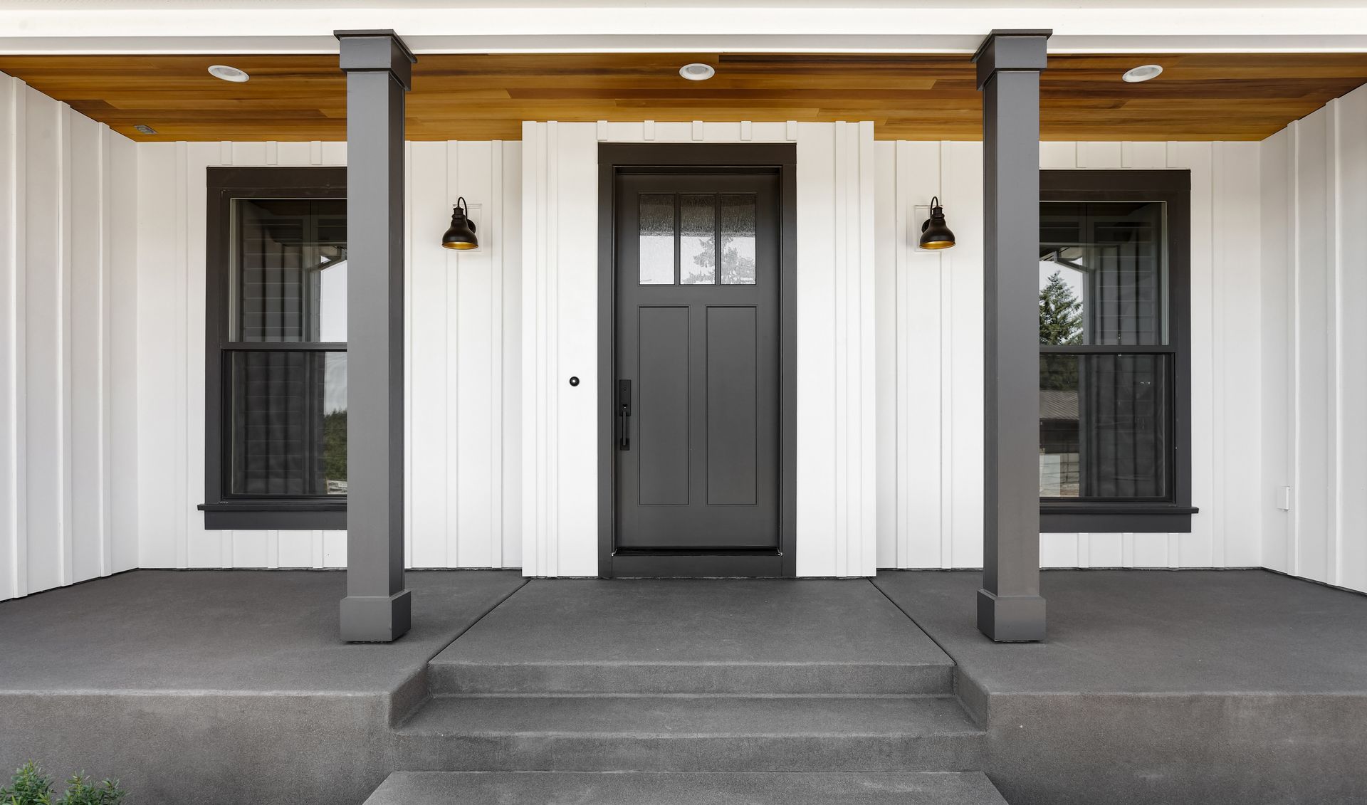 Gray front door with sidelights, porch with columns, and board-and-batten siding.