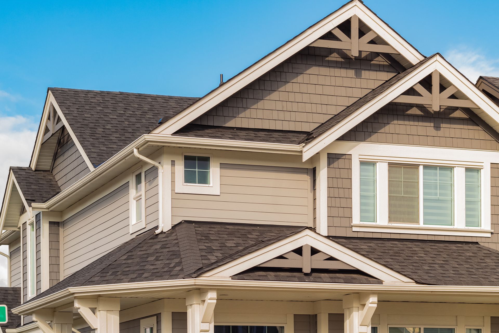 Two-story house with brown roof and light brown siding, white trim, and a blue sky.