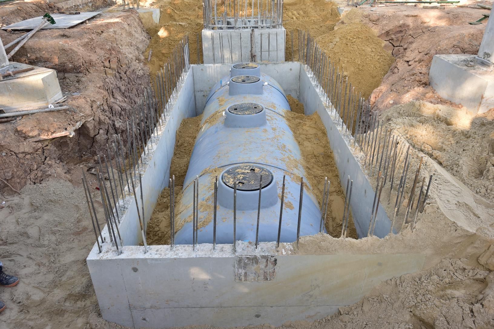 A light blue cylindrical storage tank placed inside a concrete retaining structure in a dirt construction site.