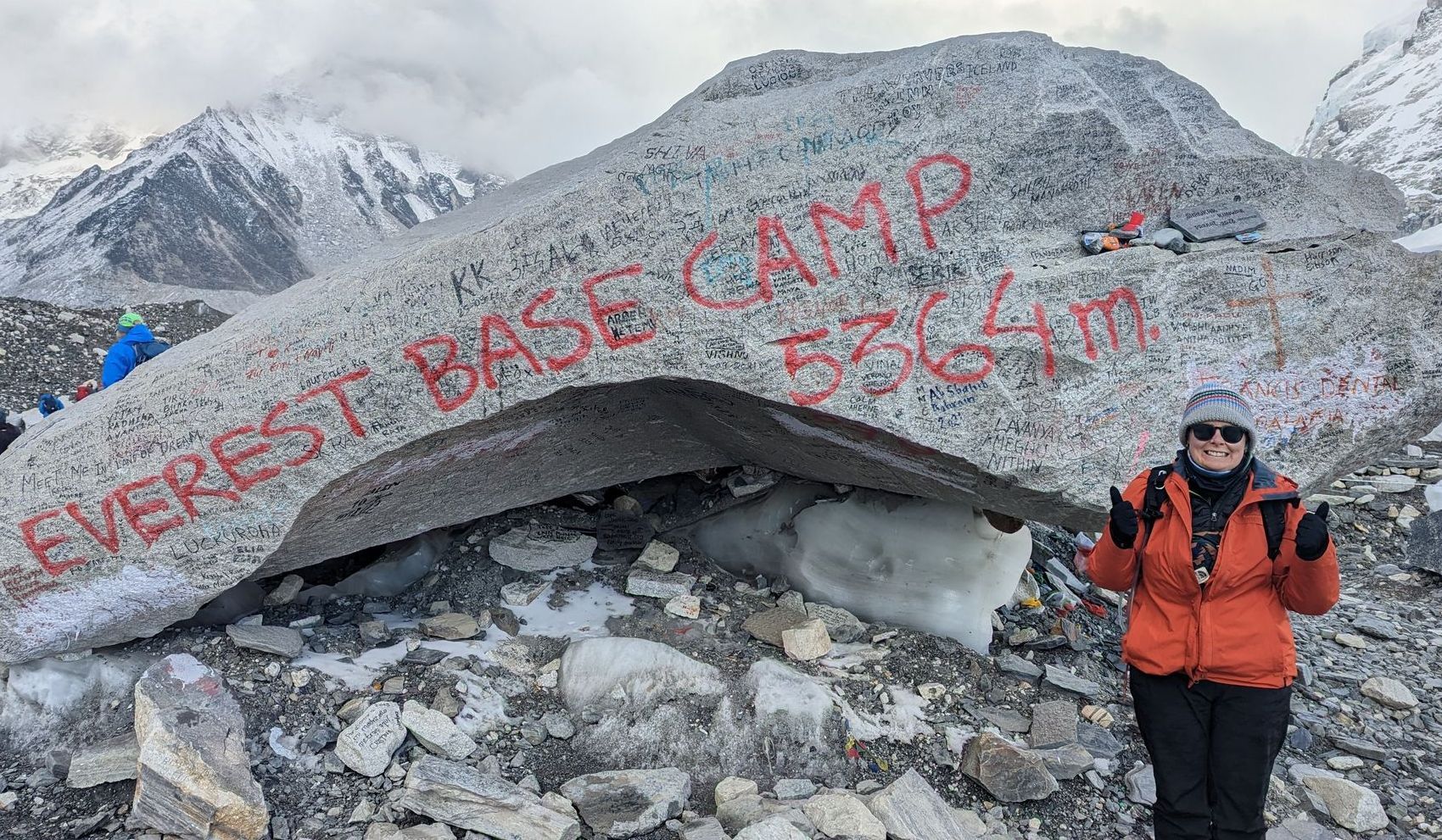 a woman is standing in front of a large rock with the words `` everest base camp '' written on it .
