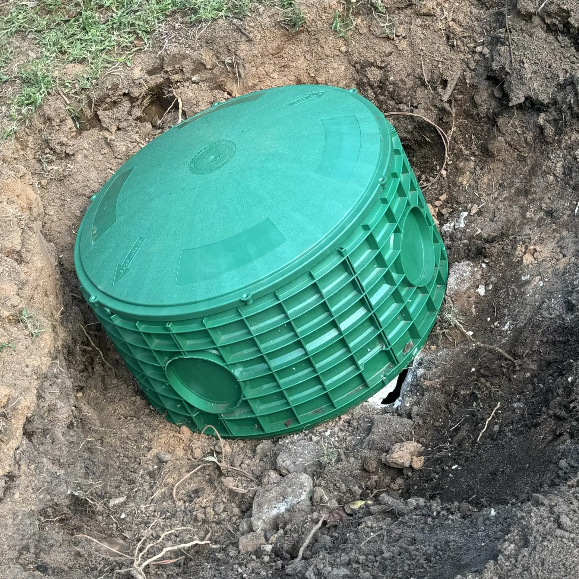 Green septic tank in an excavated hole, ready for installation.