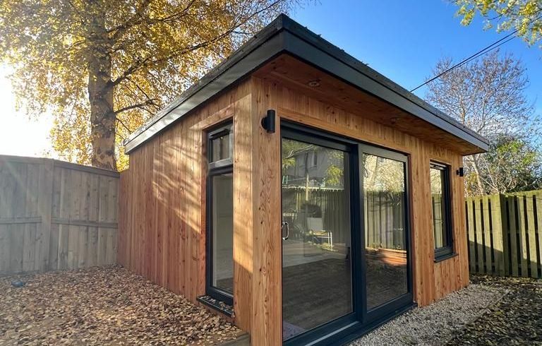 Modern 6m x 5m garden gym room in Bearsden with 1.5m roof overhang to sides, 2m deep composite decking, exterior sockets, and 3kW infrared outdoor heater.