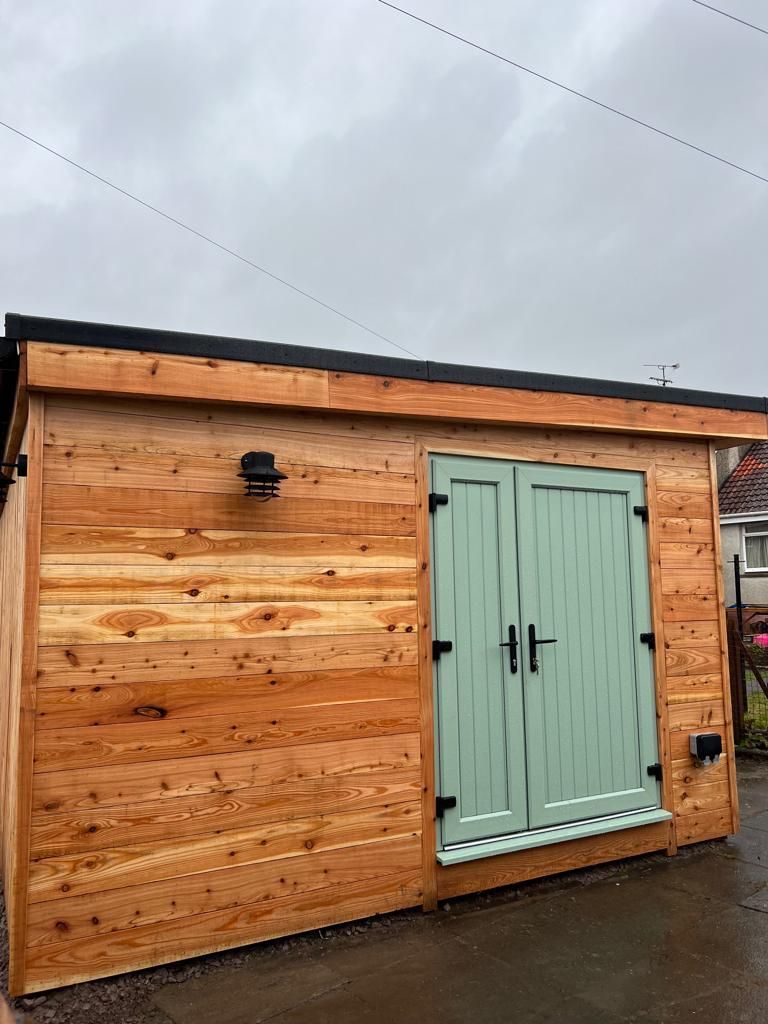 a wooden garden building with green doors and shutters