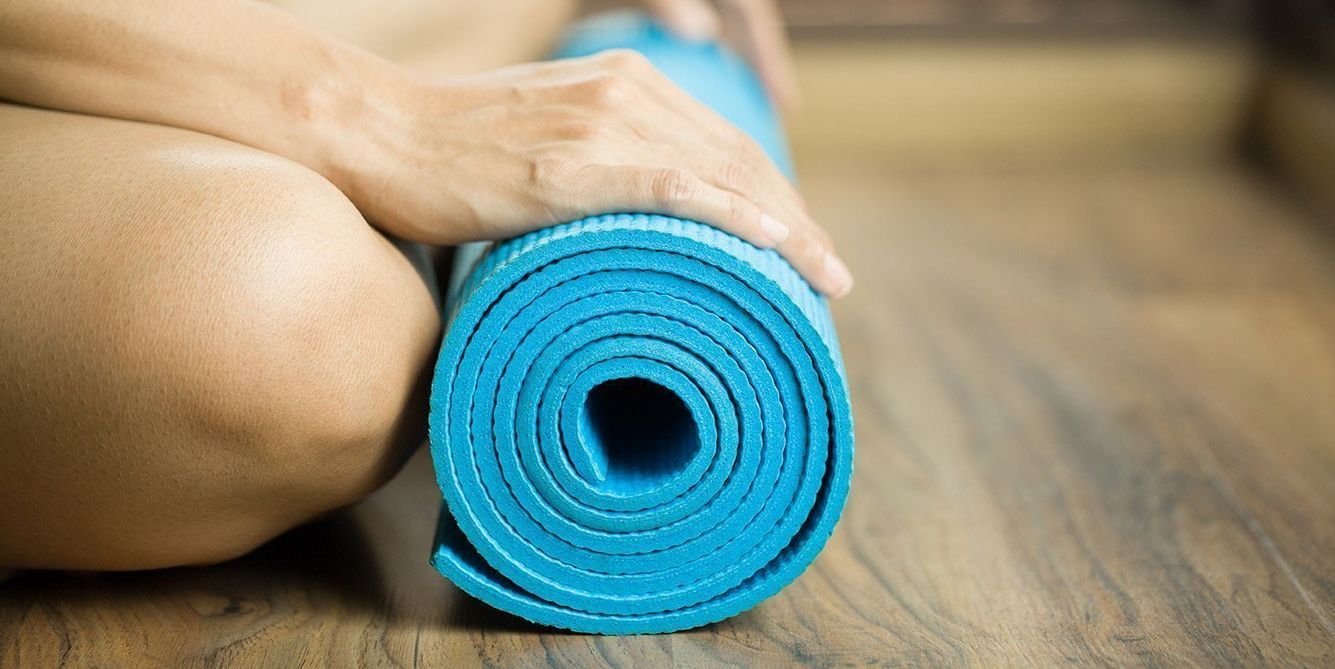 a person is sitting on the floor holding a blue yoga mat .