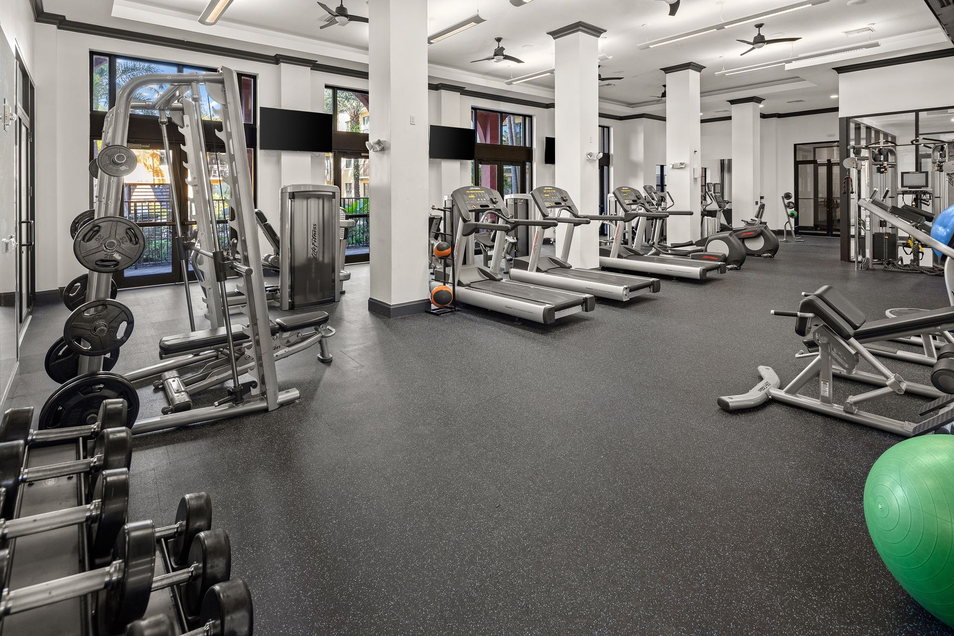A large gym filled with treadmills , dumbbells , and a green ball.