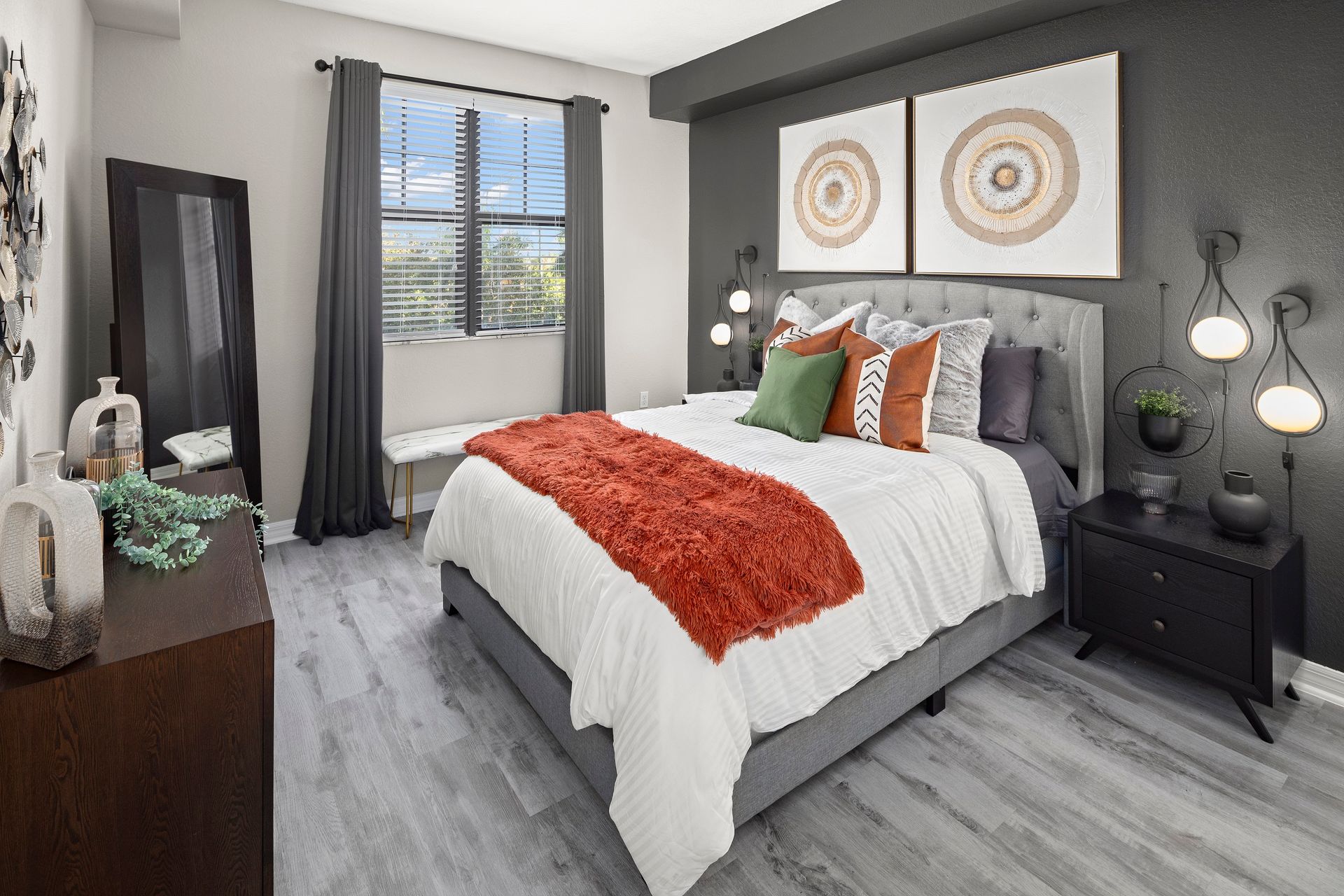 A bedroom with a bed , nightstand , mirror and window.