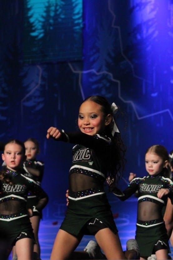 Young cheerleaders in black uniforms performing on stage; smiling, focused.