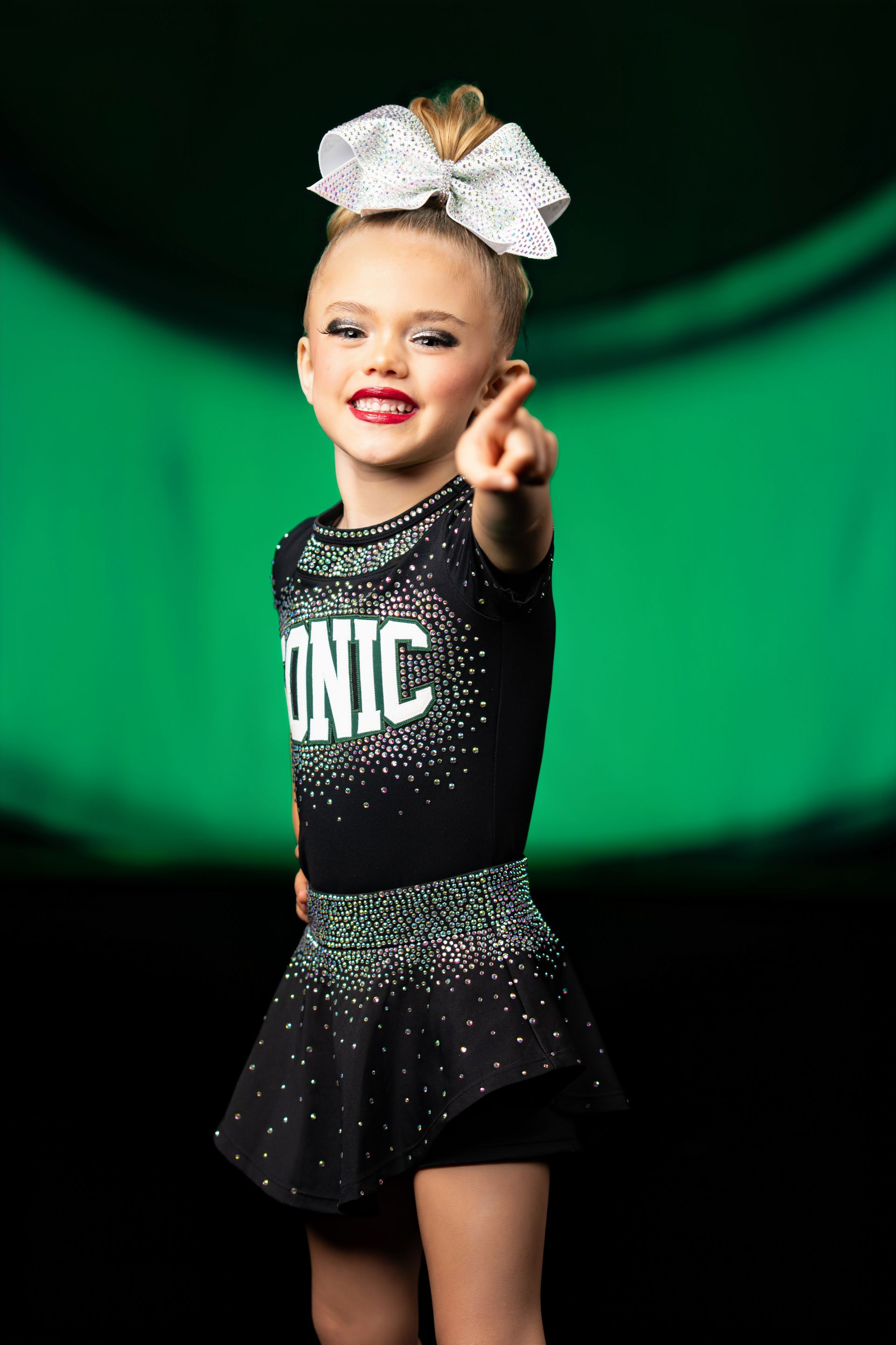 Young cheerleader atop teammates in dark green uniform, arms raised.