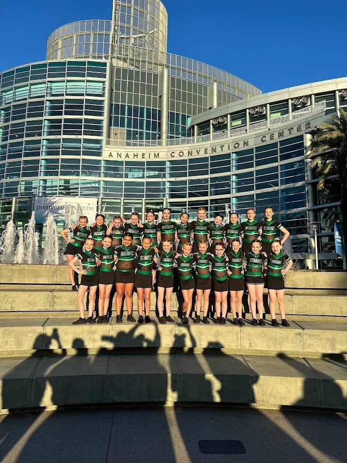 Group of young women in green and black uniforms posing in front of the Anaheim Convention Center.