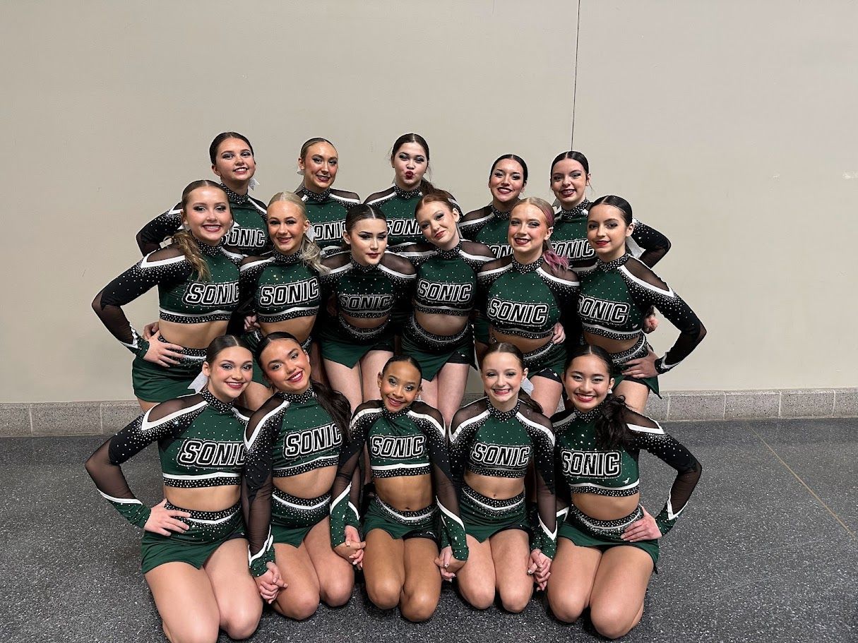 Cheerleading team in green and black uniforms, posing indoors.