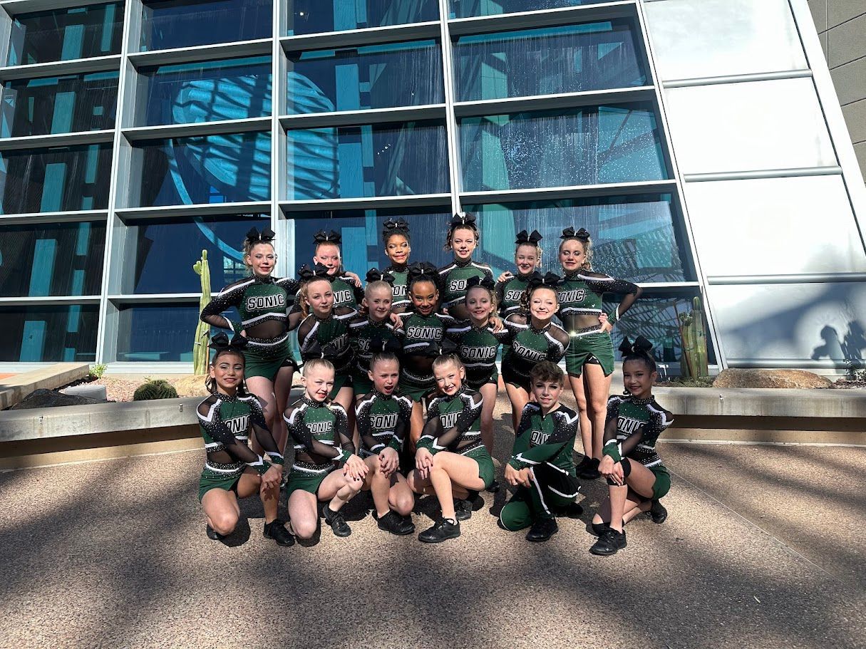 Cheerleading team in green and white uniforms poses outside a building.