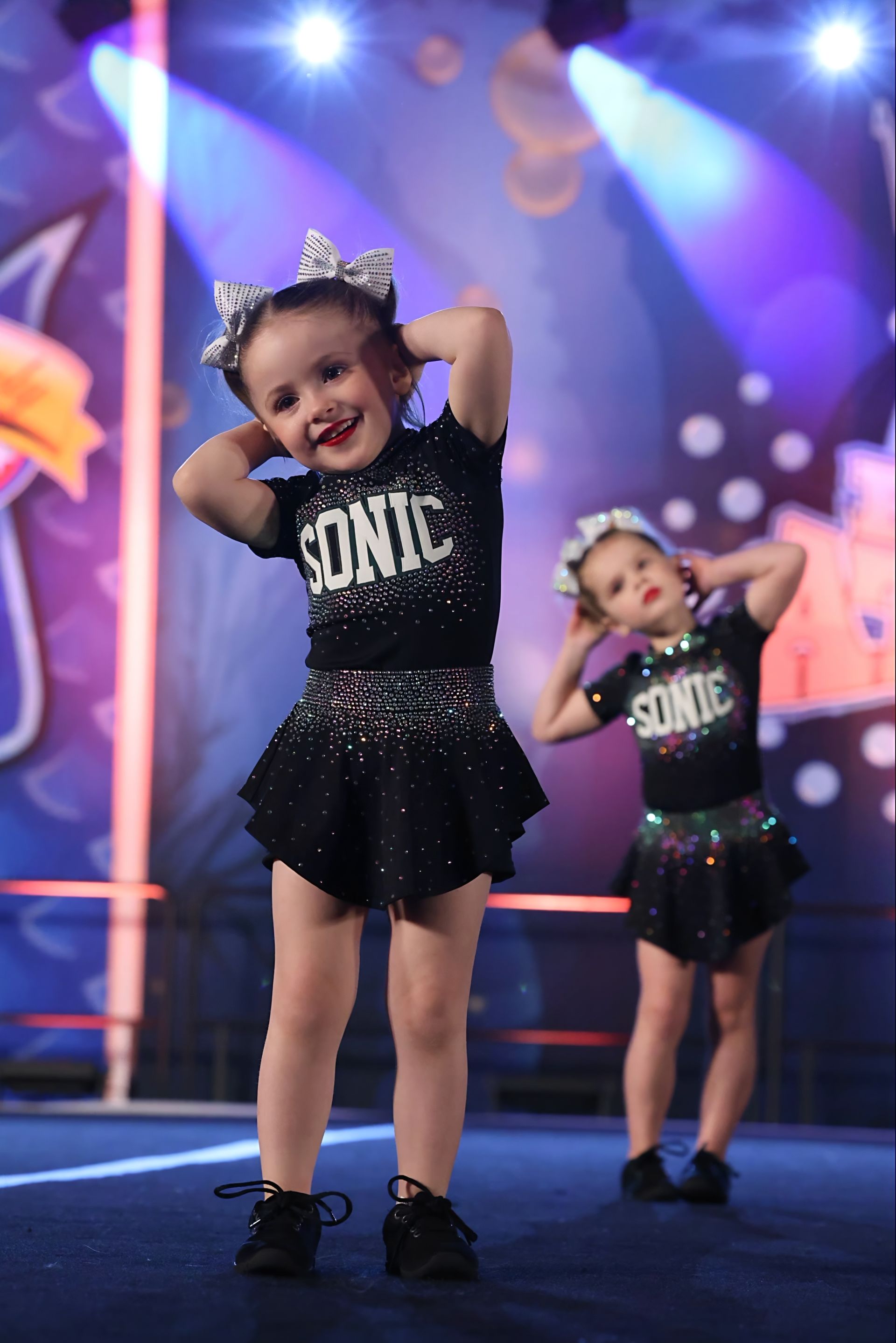 Young cheerleaders in black uniforms performing on stage; smiling, focused.