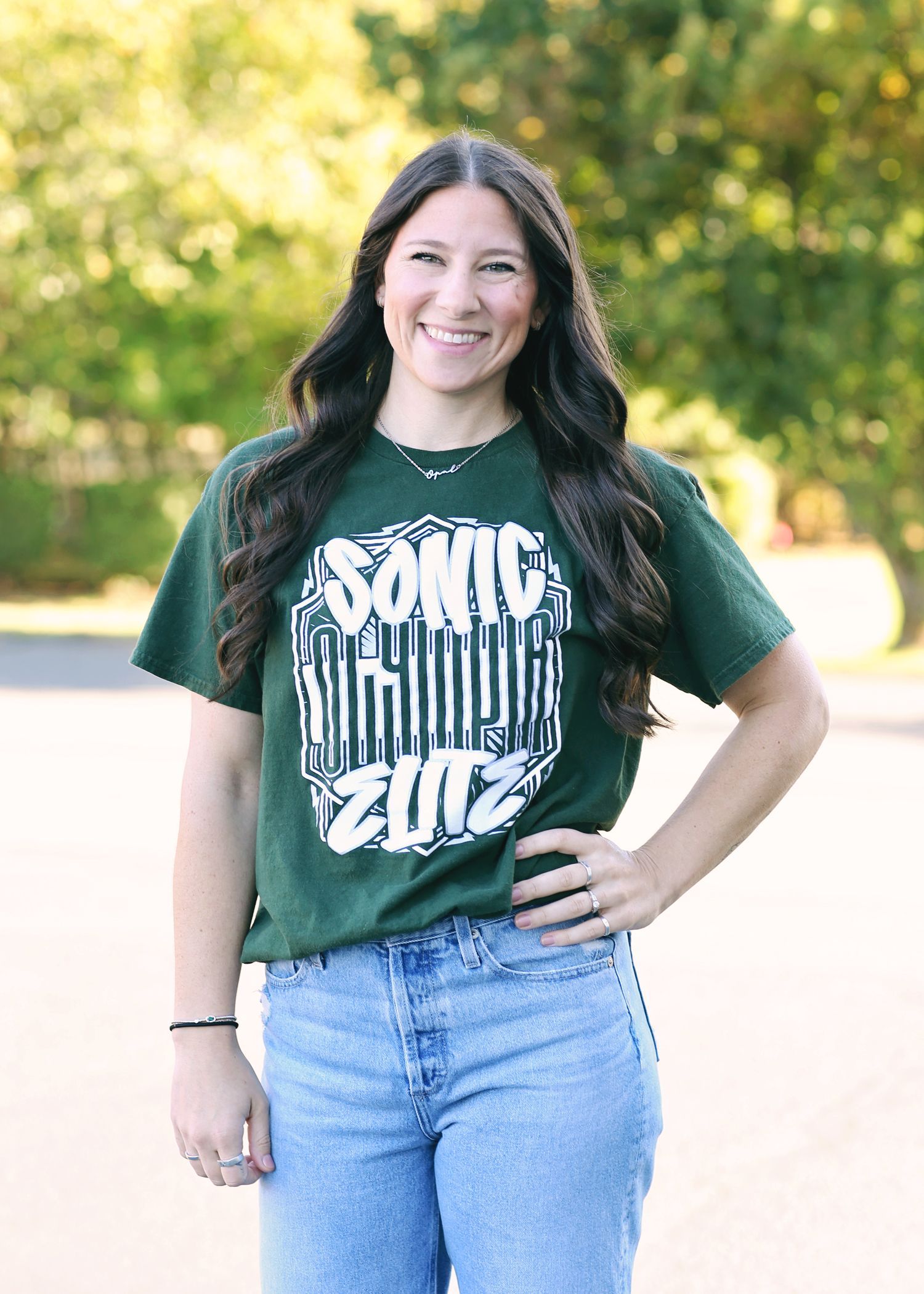 Woman in green t-shirt and jeans smiles outdoors. T-shirt has
