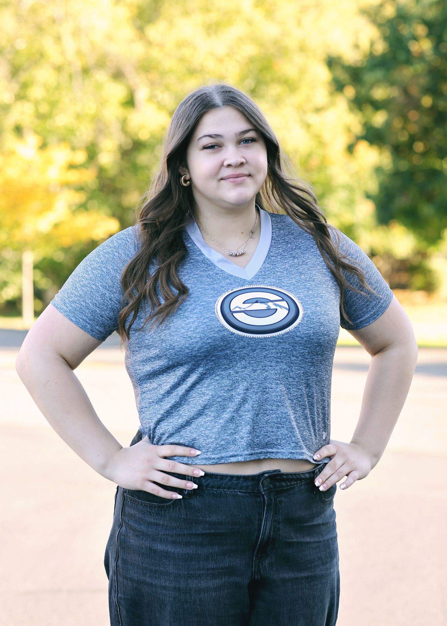 Woman with hands on hips wearing a blue graphic t-shirt and dark jeans outdoors.