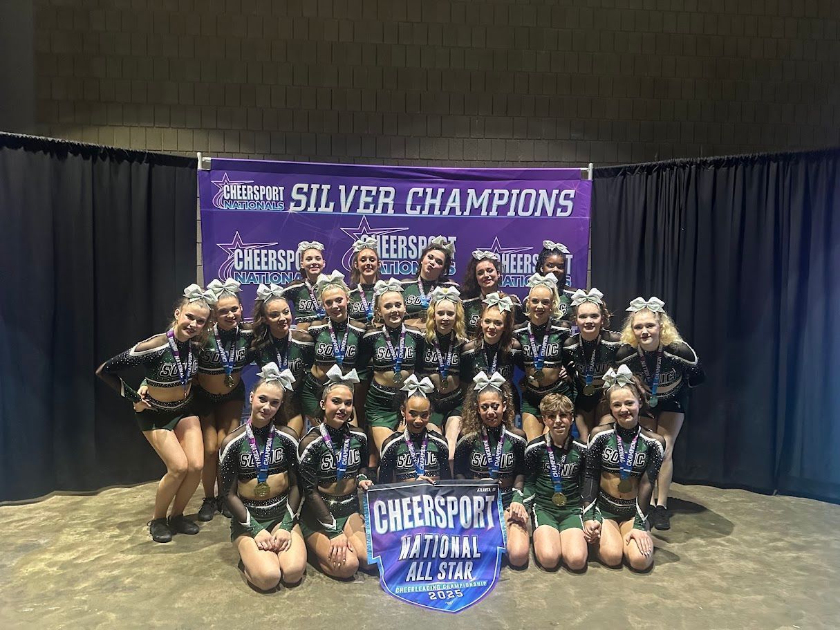 Cheerleading team posing with a banner, wearing green and black uniforms. Silver Champions banner displayed.