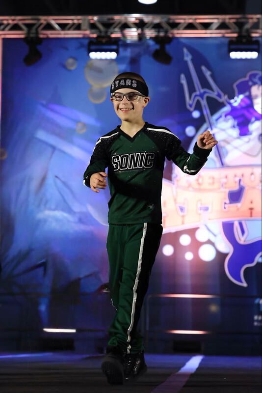 Young man in green Sonic uniform, smiles on stage.