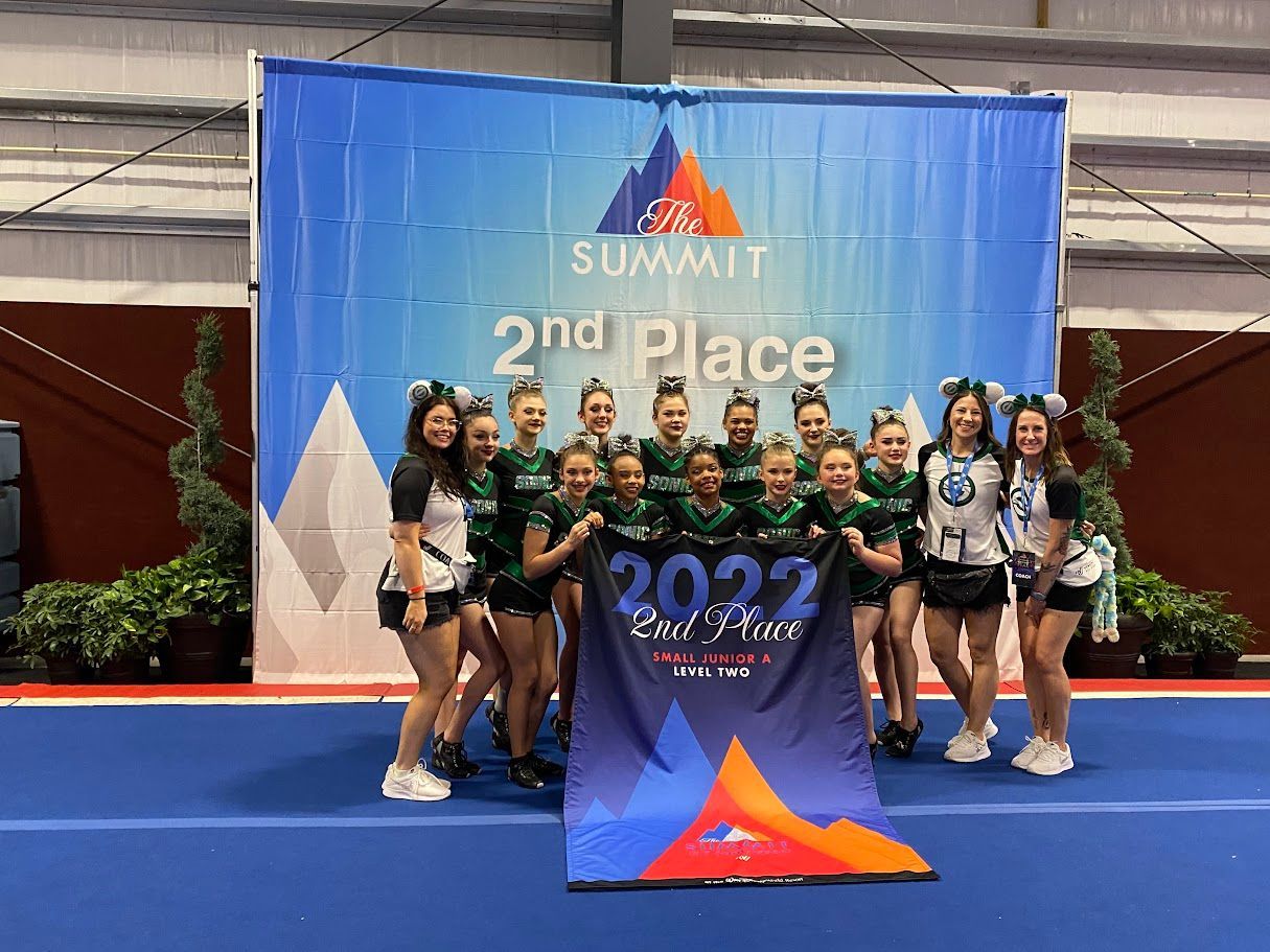 A cheerleading team in green and black uniforms holding a second-place banner at the 2022 Summit competition.