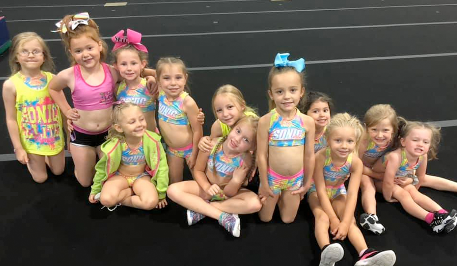 Young cheerleaders in matching swimsuits and bows, smiling on a mat.