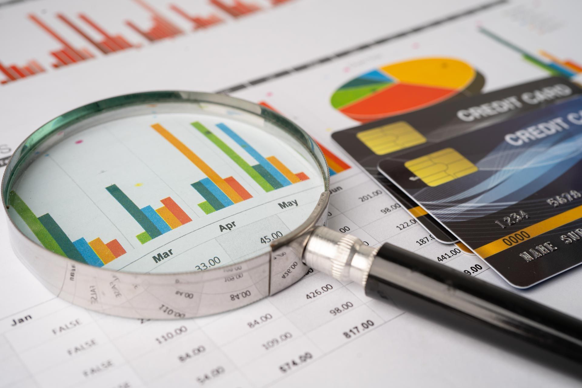 Magnifying glass over financial charts and credit cards showing data analysis. Magnifying glass over financial charts and credit cards showing data analysis.