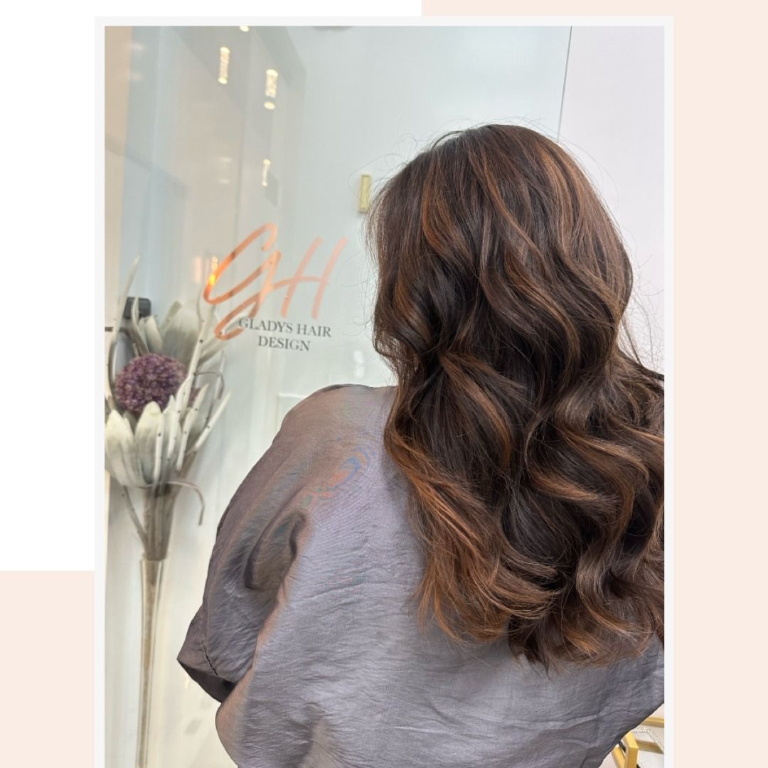 A woman with long brown hair is standing in front of a window.