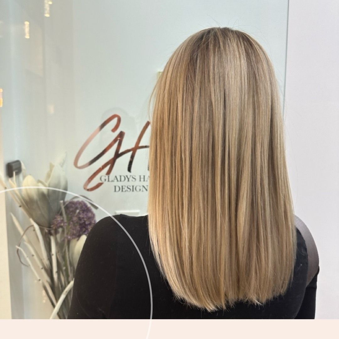 A woman with long blonde hair is standing in front of a sign for gladys hair design