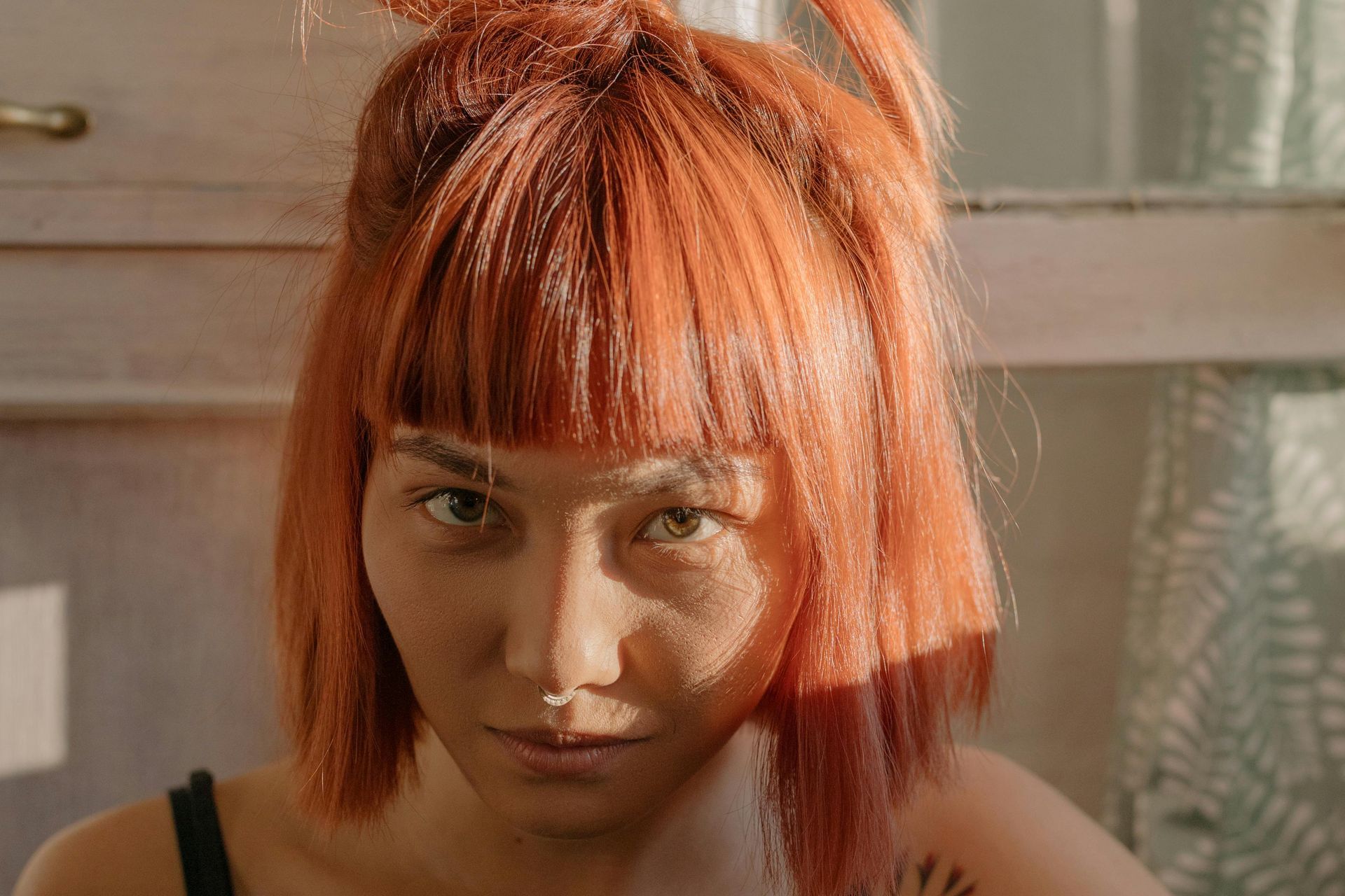 A woman with red hair and a nose ring is looking at the camera.
