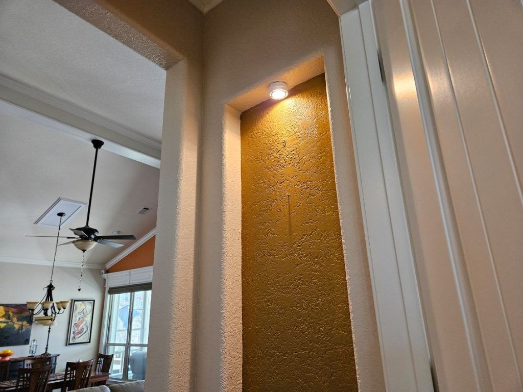 Niche with gold-colored mosaic tile, lit from above. Flanked by white and textured beige walls.