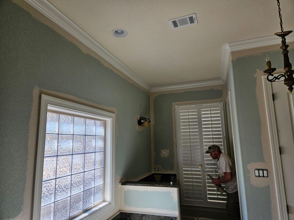 Man in bathroom painting walls; green walls, white trim, glass block window.
