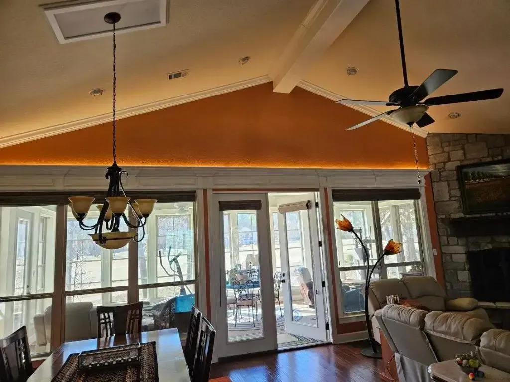 Dining room with chandelier, French doors, and a ceiling fan. Orange wall and a stone fireplace.